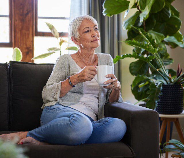 Older woman enjoying a cup of coffee on her couch.