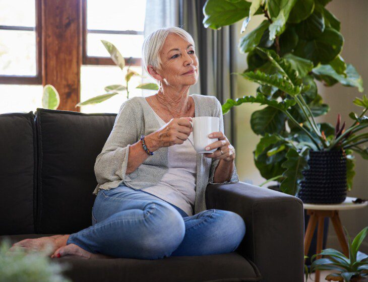 Older woman enjoying a cup of coffee on her couch.